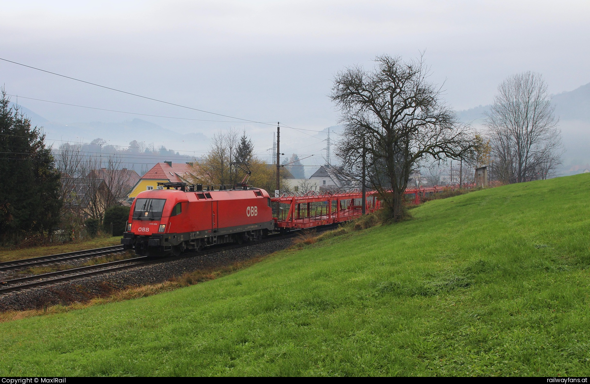 ÖBB 1116 085 in Lahrndorf - Der herbstliche Nebel liegt am 26.11.2024 über dem Ennstal als hier in Lahrndorf die 1116 085 mit einem leeren Autozug von Villach Süd Gvbf nach München Nord Rbf auf die Zugkreuzung mit einem Regionalzug wartet.  Rudolfsbahn | St.Valentin - Kastenreith Railwayfans