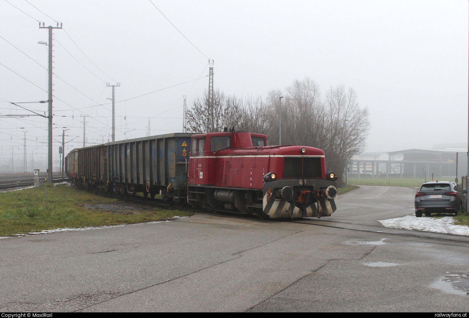 Agrana V81 in Enns - In einem engen Bogen bei leichtem Gefälle kreuzt die Anschlussbahn der Agrana Enns die Westbahnstraße über die hier am 6.1.2025 die ehemalige SLB V81 mit einigen leeren Wagen zum Rübenplatz im Bereich der ehemaligen Zuckerfabrik fährt.   Railwayfans