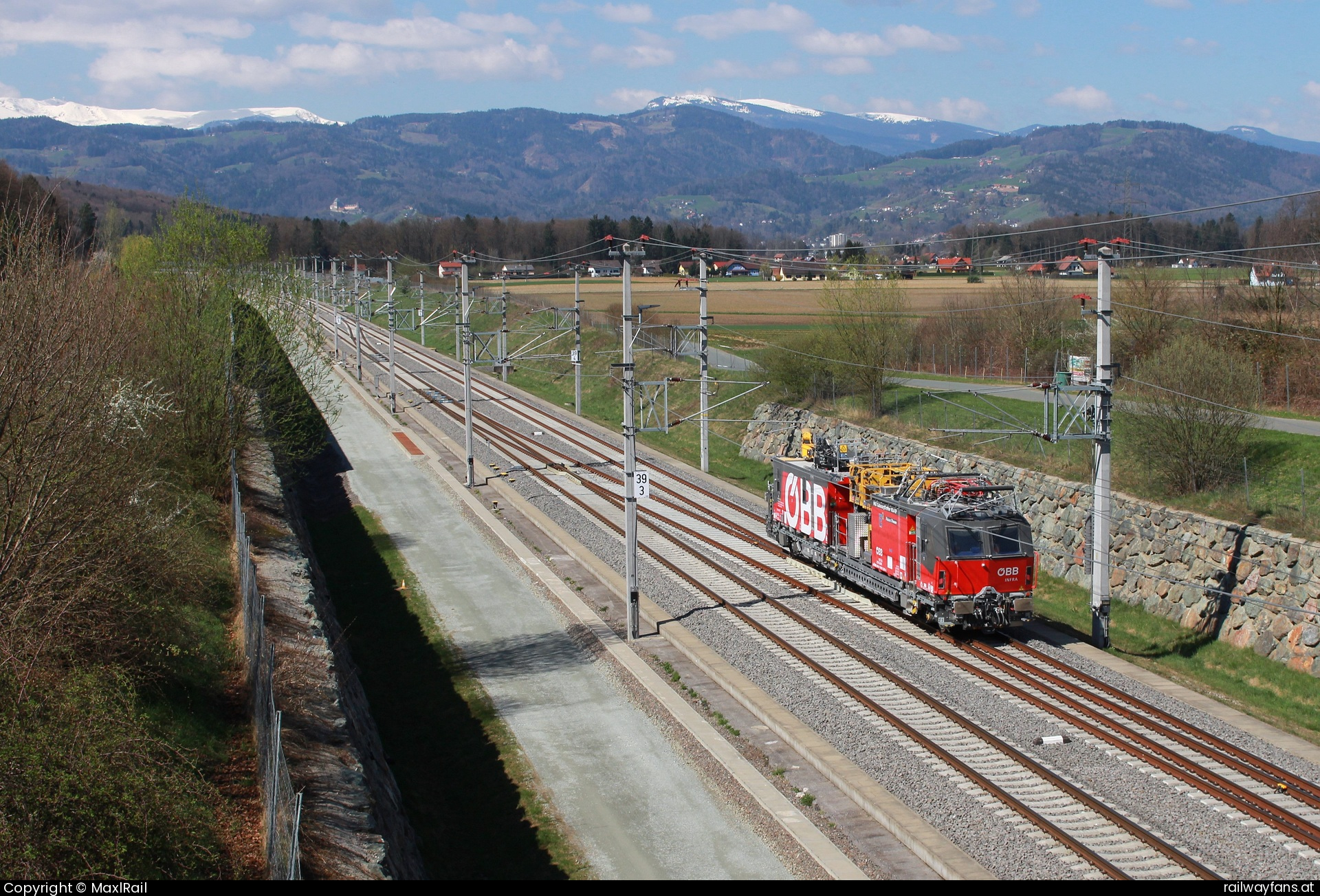 ÖBB X710.201 in Lebing - Eine Brücke beim Bahnhof Weststeiermark bietet einen herrlichen Panoramablick auf die Koralpe sowie links über der Oberleitung die Burg von Deutschlandsberg.
Der neue X710.201, ein Plasser&Theurer Catenary Crafter 15.4 E3, fährt hier am 3.4.2025 aus dem Bahnhof Weststeiermark in Richtung Kärnten.  Koralmbahn Railwayfans