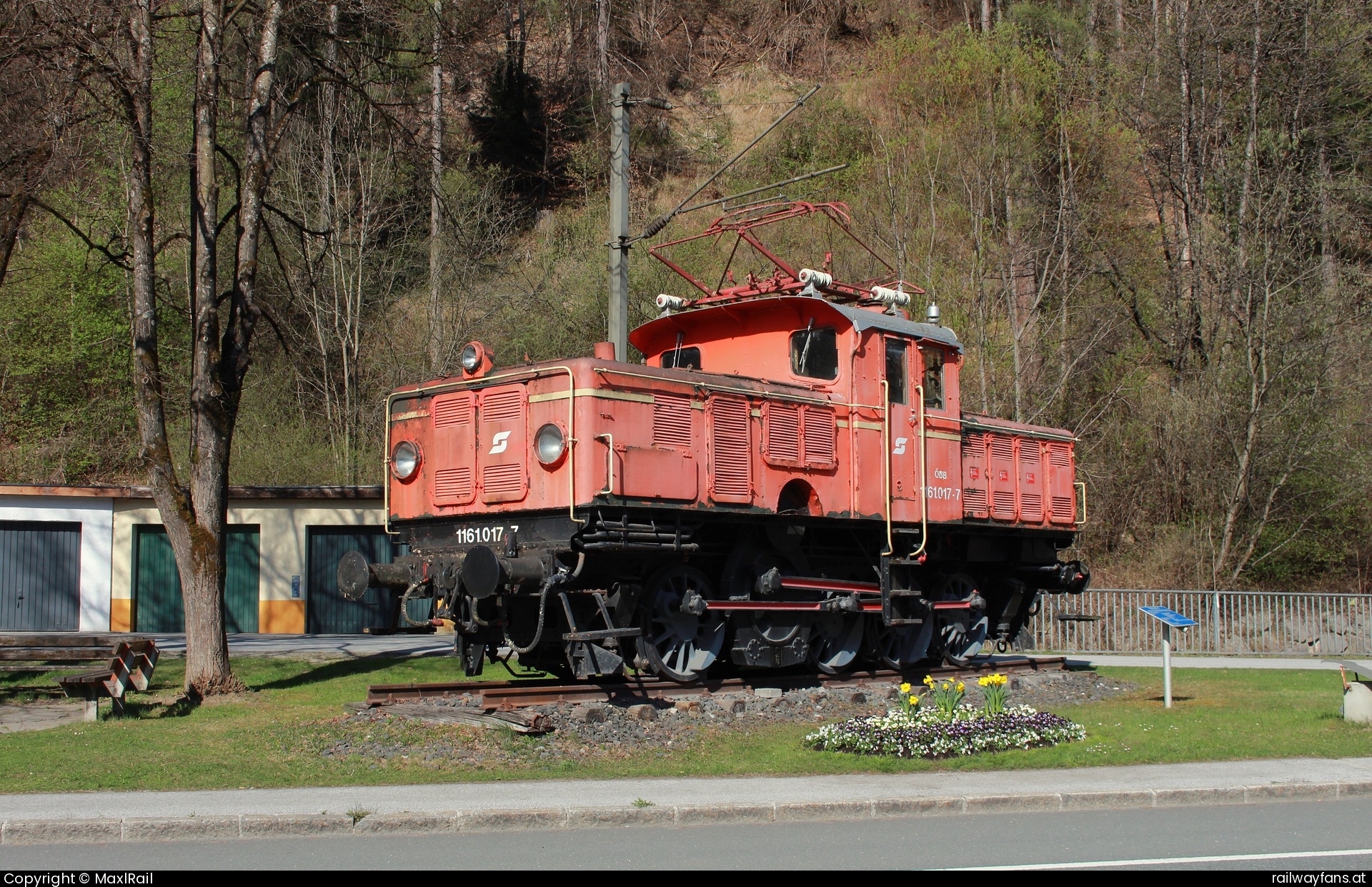 ÖBB 1161 017 in Laideregg - Tagtäglich war die, ab 1928 gebaute Lokreihe 1161 im Salzburger Pongau im Verschub tätig. Ihr markantes erscheinungsbild sowie das Fahrgeräusch des Schrägstangenantriebs haben diese Verschublok weithin bekannt gemacht. Seit 1993 ist die 1161 017 ausgemustert, wurde 1994 äußerlich restauriert und erhielt ihre ursprüngliche Lackierung in grün. Seit dem steht sie am Ortsanfang von Bischofshofen, erhielt allerdings 2013 oder 2014 eine blutorange Lackierung. Bei herrlichem Sonnenschein am 8.4.2025 ruht die betagte E-Lok auf ihrem Sockel verziert von einigen Blumen.   Railwayfans