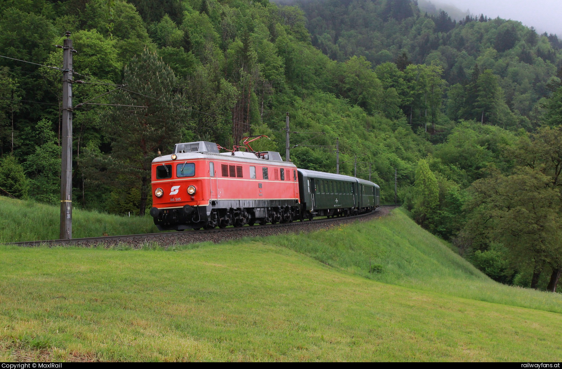 Pro Bahn Vorarlberg 1110 505 in Innerbraz mit dem SLP 14496 - Zwischen Hintergasse und Braz wird die 30‰ Neigung gut sichtbar als hier am regnerischen 5.5.2025 die 1110.505 mit einem Personenzug talwärts rollt.
Die starke E-Bremse der schweren Güterzuglok zahlt ist hier auf alle Fälle von Vorteil.  Arlbergbahn Railwayfans