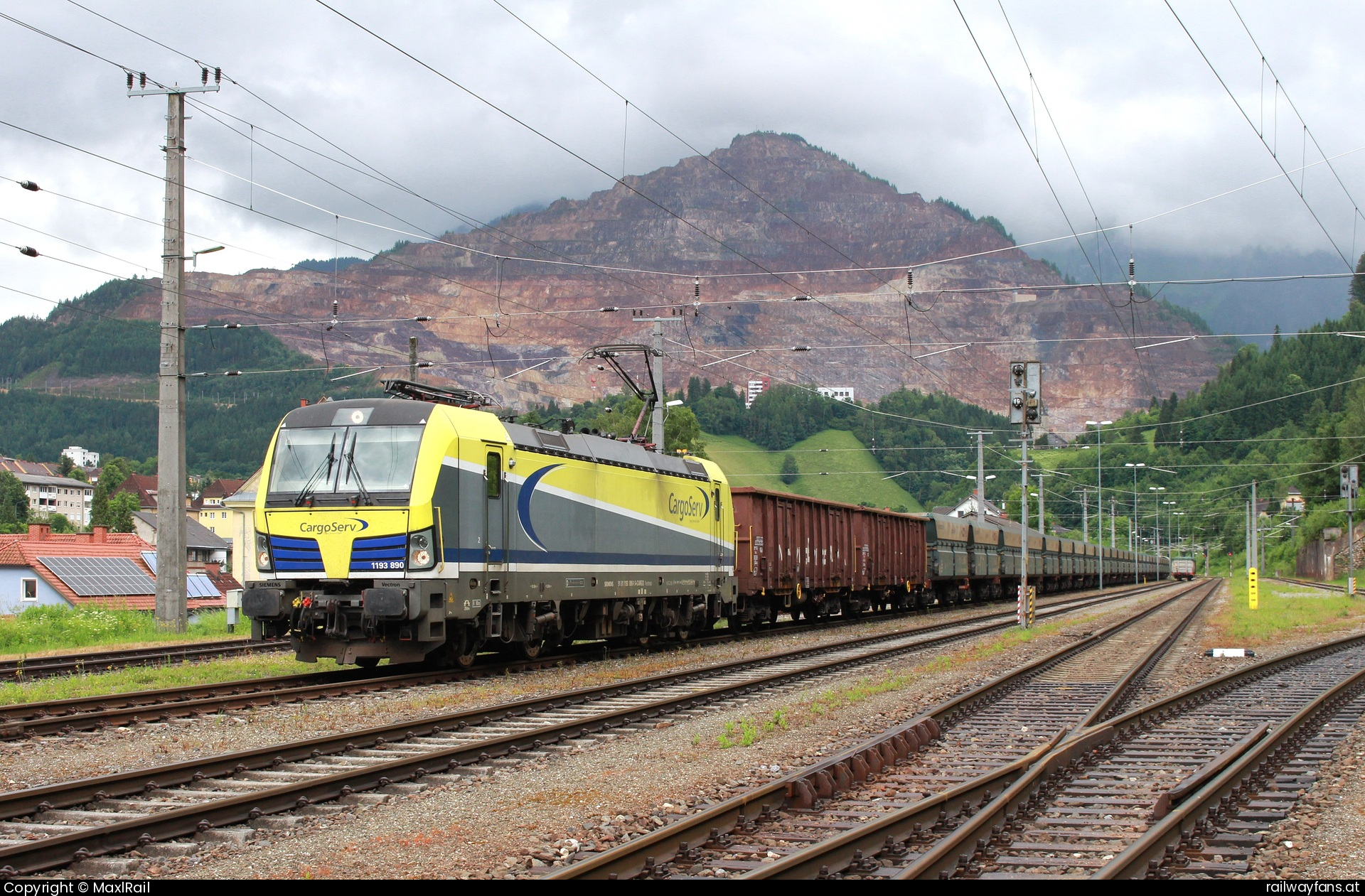Cargoserv 1193 890 in Eisenerz - Am Fuße des steirischen Erzberges liegt die Stadtgemeinde Eisenerz die seit Beginn des Erzabbaus vom Bergbau geprägt ist.
Am Rande der Stadt liegt auch der gleichnamige Bahnhof.
Am 16.6.2025 wartet die 1193 890 der CargoServ mit einem leeren Erzzug von Linz Stahlwerke her auf die Verschubfahrt nsch Krumpental, wo der Ganzzug mit Feinerz aus Siderit und Dolomit beladen wird.
Bis 1984 erfolgte die Verladung des Erzes im Bahnhof Eisenerz, das Material wurde mit einer Schmalspurbahn, dem 